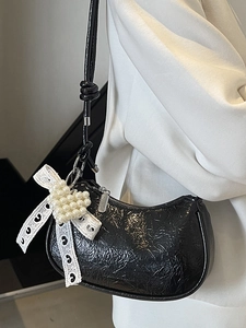 Glossy black hobo bag with white lace bow and pearl heart charm on model