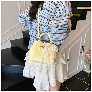 Detail showing pale yellow leather bucket bag with white lace bow and pearl pendant