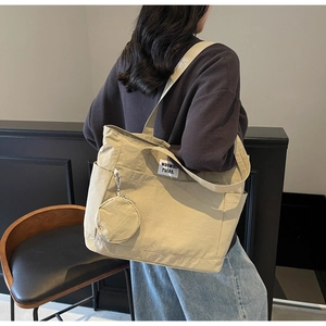 Detail of beige canvas tote bag with hanging round coin purse and white brand label