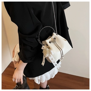 Détail du mini sac seau blanc avec poignée en métal argenté et breloque en dentelle