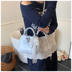 Detail of light blue bucket bag with white lace bow and pearl charm worn by a model