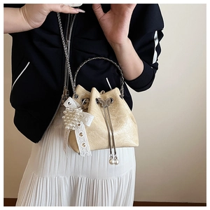 Détail d'un sac seau jaune crème avec une poignée ronde en métal et un charm papillon perlé
