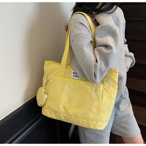Detail of a bright yellow tote bag with textured fabric, mini pouch, and textile label