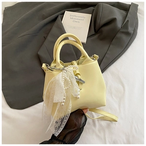 Detail of cream bucket bag featuring elegant lace scarf and pearl pendant accents