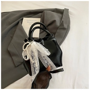 Detail of black patent leather bucket bag featuring white lace and pearl bow charm