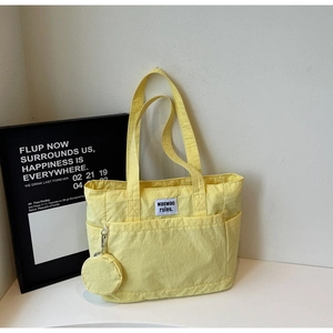 Detail of bright yellow canvas tote bag featuring square logo patch and small round coin purse