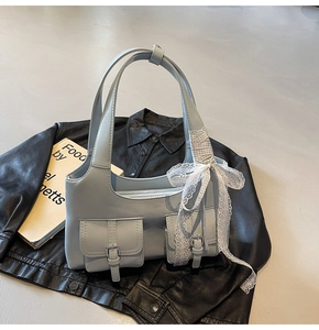 Dettaglio borsa tote azzurra con fiocco in pizzo bianco e fibbie argentate su giacca nera