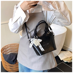 Detailansicht der schwarzen Lackleder-Eimertasche mit Spitzenschleife und Perlenkette