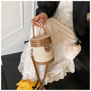 Dettaglio borsa a secchiello intrecciata beige con manici in pelle marrone e catena