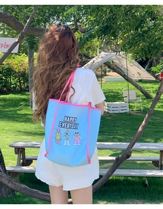 Outdoor view of a blue tote bag with cartoon embroidery and HAPPY EVERYDAY text