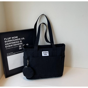 Detail view of black canvas tote bag with small round pouch and stylish brand label