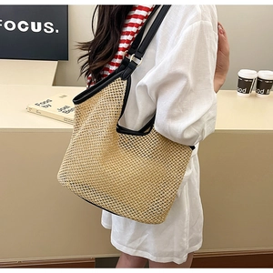 Detail of woven straw tote bag featuring black leather trim and metallic buckles