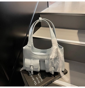 Dettaglio della borsa tote azzurra con tasche a patta e decorazione a nastro di pizzo