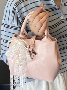 Pink bucket bag with pearl bow accessory and top handle shown in lifestyle context