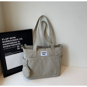 Detail view of large khaki canvas tote bag with hanging round coin purse and logo patch