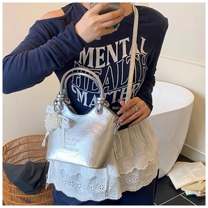 Detail der silbernen Metallic-Eimertasche mit Perlenriemen und Spitzen-Schleifen-Anhänger