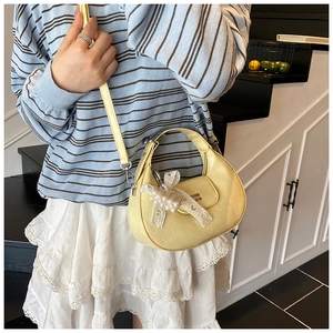 Détail du sac bandoulière demi-lune jaune clair avec nœud en dentelle et logo en métal