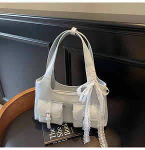 Dettaglio della tote in pelle azzurra con due tasche frontali e un fiocco di pizzo bianco