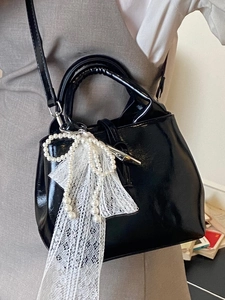 Glossy black bucket bag with a pearl lace bow charm and crossbody strap for women