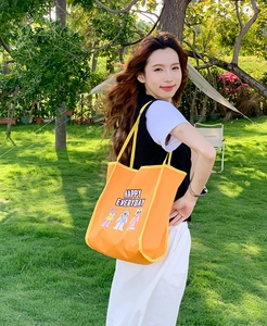 Outdoor shot of bright orange tote bag with cartoon embroidery and HAPPY EVERYDAY text