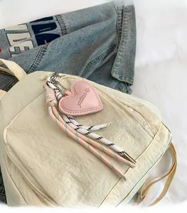 Détail du sac à dos en nylon blanc crème avec breloque cœur rose et cordon tressé