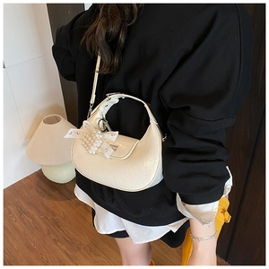 Détail d'un sac demi-lune beige avec texture plissée brillante et pendentif en perles