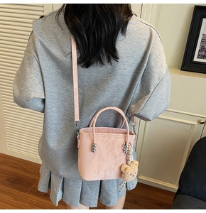 Close-up of pink pleated bucket bag with cute plush bear charm and slender strap
