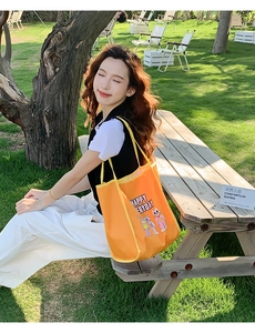 Detail of vibrant orange canvas tote bag with cartoon print and long yellow straps