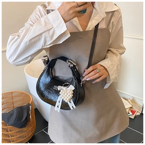 Détail du sac bandoulière croissant noir avec texture plissée et breloque perle cœur