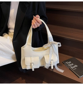 Dettaglio della borsa a spalla color crema con fiocco in pizzo e tasche con fibbia