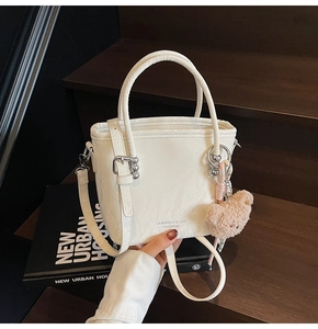 Detail of white embossed bucket bag with a cute brown teddy bear plush charm