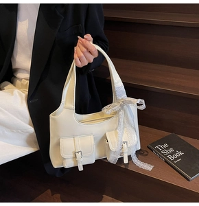 Dettaglio di una borsa tote bianco crema con due fibbie sulle tasche e un fiocco in pizzo