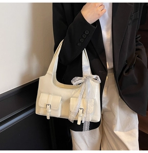 Dettaglio della borsa tote crema con tasche cargo e fiocco in pizzo su blazer nero