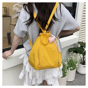 Détail du sac à dos en nylon jaune avec pendentif cœur porté par un mannequin dehors