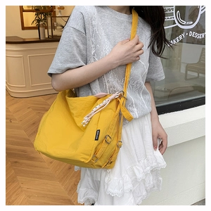 Détail du sac bandoulière en nylon jaune avec étiquette tissée et breloques colorées