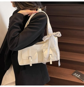 Dettaglio borsa sottospalla crema con tasche a patta e decorazione con fiocco in pizzo