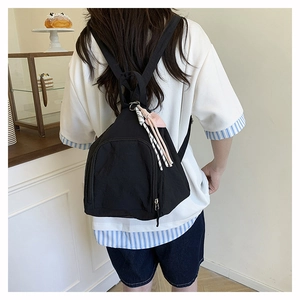 Détail d'un mini sac à dos en nylon noir avec breloque cœur rose et glands tressés