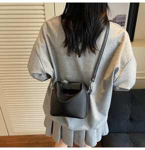 Detailed back view of a black lychee pattern leather bucket bag with silver hardware on a model