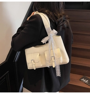 Dettaglio della borsa sottobraccio crema con tasche decorative e fiocco in pizzo