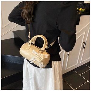 Detail of a beige cylinder crossbody bag with lace bow and pearl pendant details