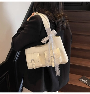 Dettaglio di una borsa tote beige lucida con fiocco a quadretti blu sulla tracolla