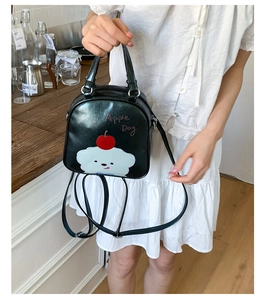 Détail de l'imprimé chiot blanc et du logo pomme rouge sur le mini sac à dos en cuir noir