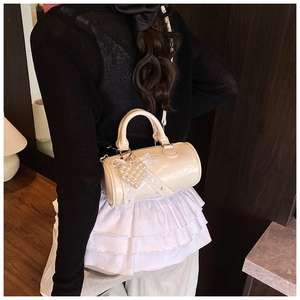 Detailed macro view of the glossy cream cylinder bag with pearl heart charm and lace detail