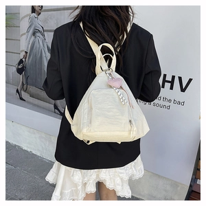 Détail du sac à dos triangulaire en nylon crème avec breloque cœur porté par le mannequin