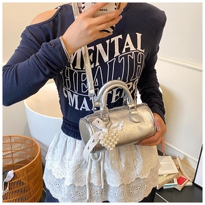 Detail view of silver cylindrical handbag with pearl heart charm and lace bow decor