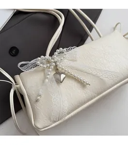 Détail du sac à aisselle crème avec nœud en dentelle, perles et pendentif cœur