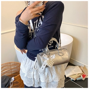Detail of silver cylinder handbag with metallic pleats and pearl heart lace charm