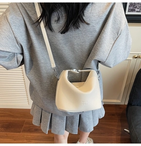 Detail of lychee textured leather crossbody bag in cream white worn by model in a room