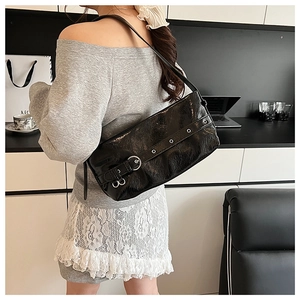 Detail of black wrinkled patent leather shoulder bag with silver eyelets and buckle