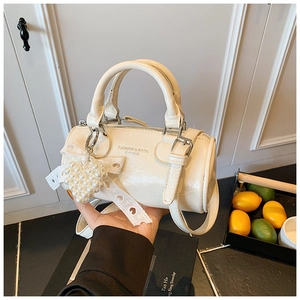 Detail view of cream cylindrical handbag with shiny texture and heart pearl charm